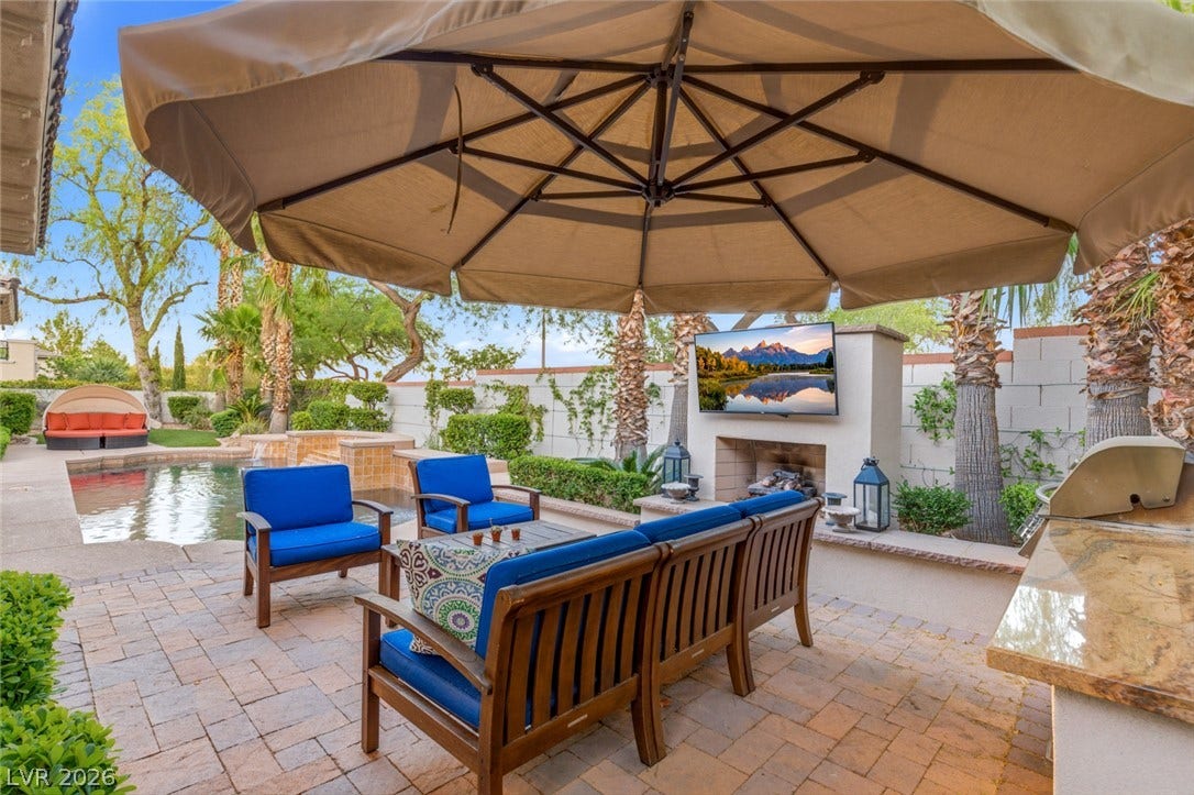 An inviting stone patio features a built-in outdoor fireplace alongside a sparkling pool.
