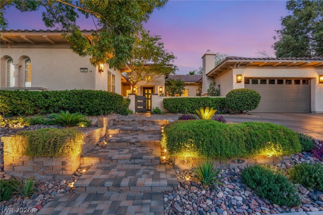 Illuminated stone pavers and manicured desert plantings lead toward a welcoming gated entryway.