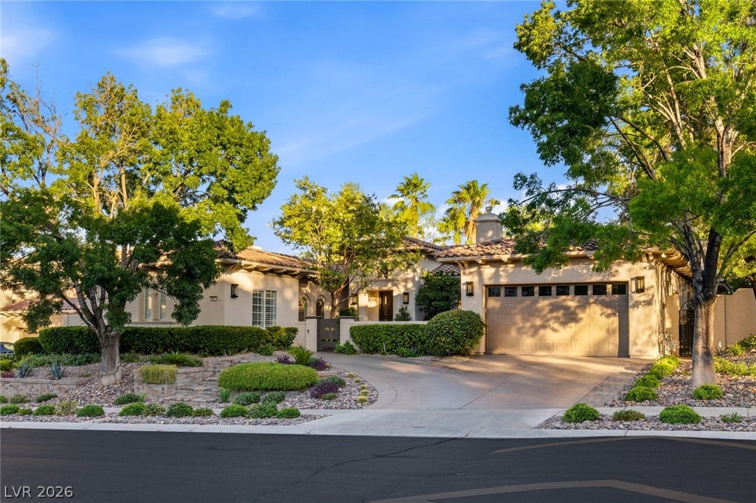 Mature trees frame the paved driveway leading to a classic stucco exterior with tile roofing.