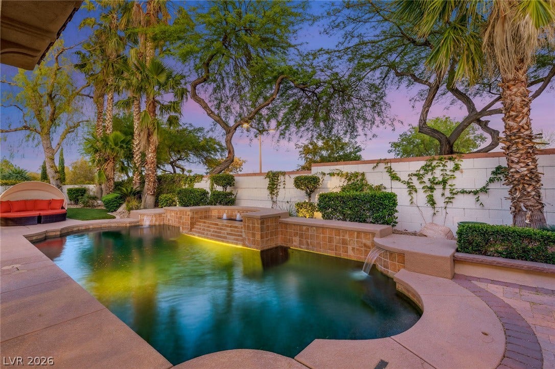 Lush palms and manicured greenery frame a custom swimming pool featuring built-in waterfalls.