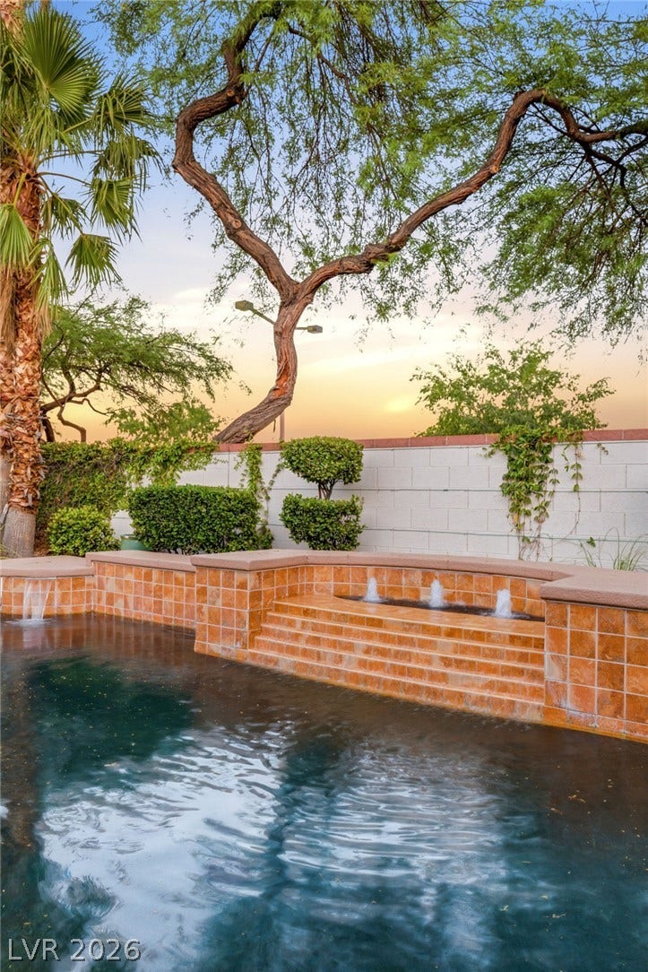 A sparkling swimming pool features integrated water fountains and warm tile accents under mature shade trees.
