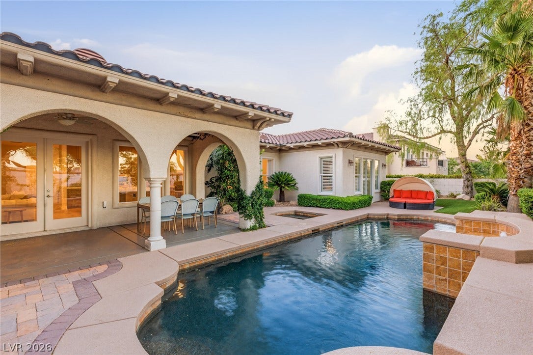 A sparkling pool anchors this Mediterranean-style backyard featuring arched patio loggias and red tile roofing.