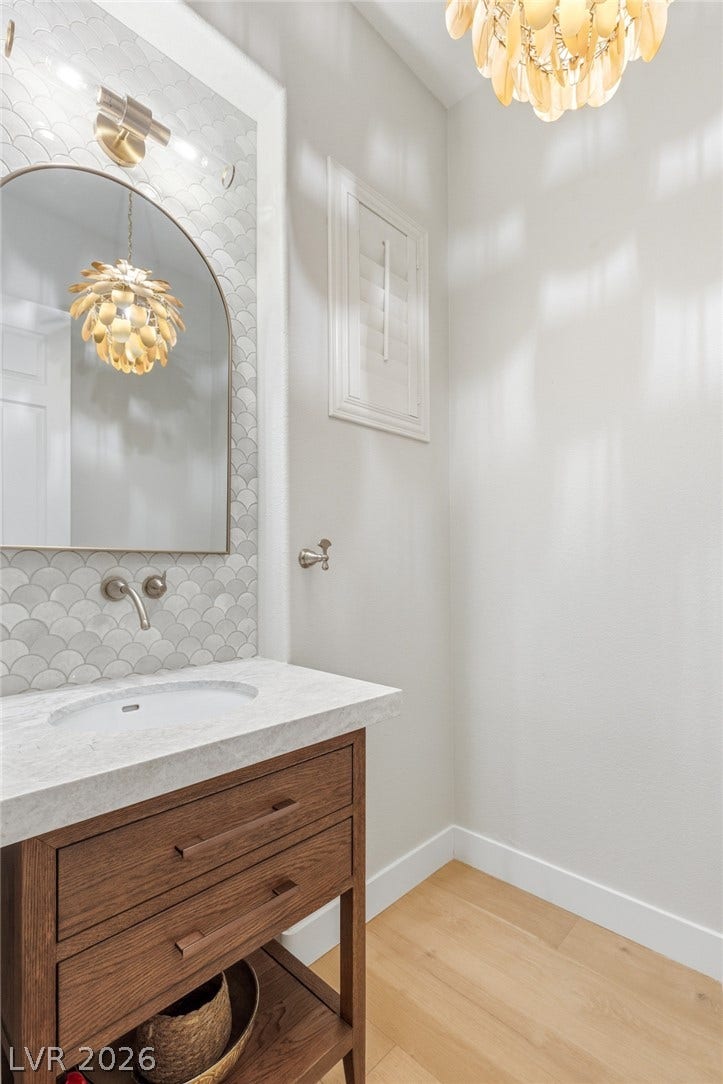 Elegant tiling and a stone counter highlight this refined powder room with warm wood floors.