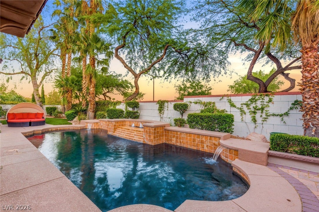 Lush tropical palm trees frame a tranquil in-ground swimming pool featuring stone accents and water spillways.