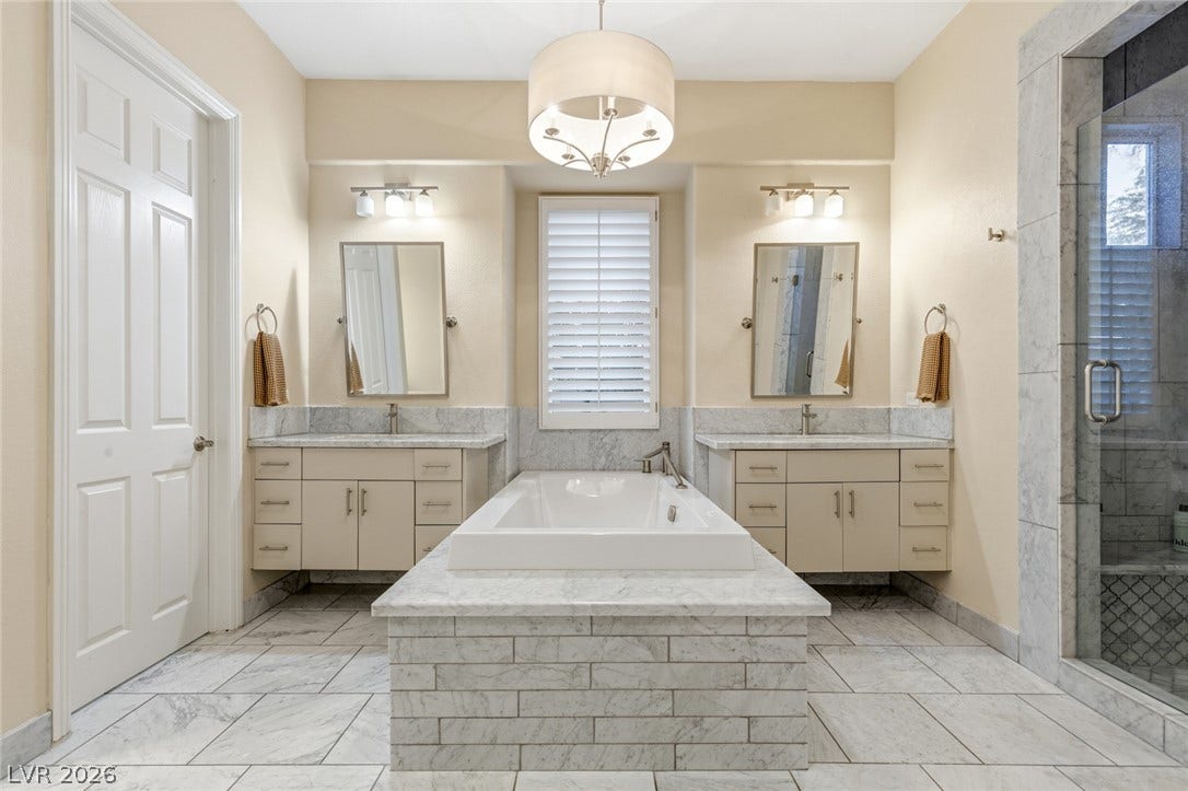 Elegant marble tile flooring and dual vanities anchor this spacious primary bath suite.