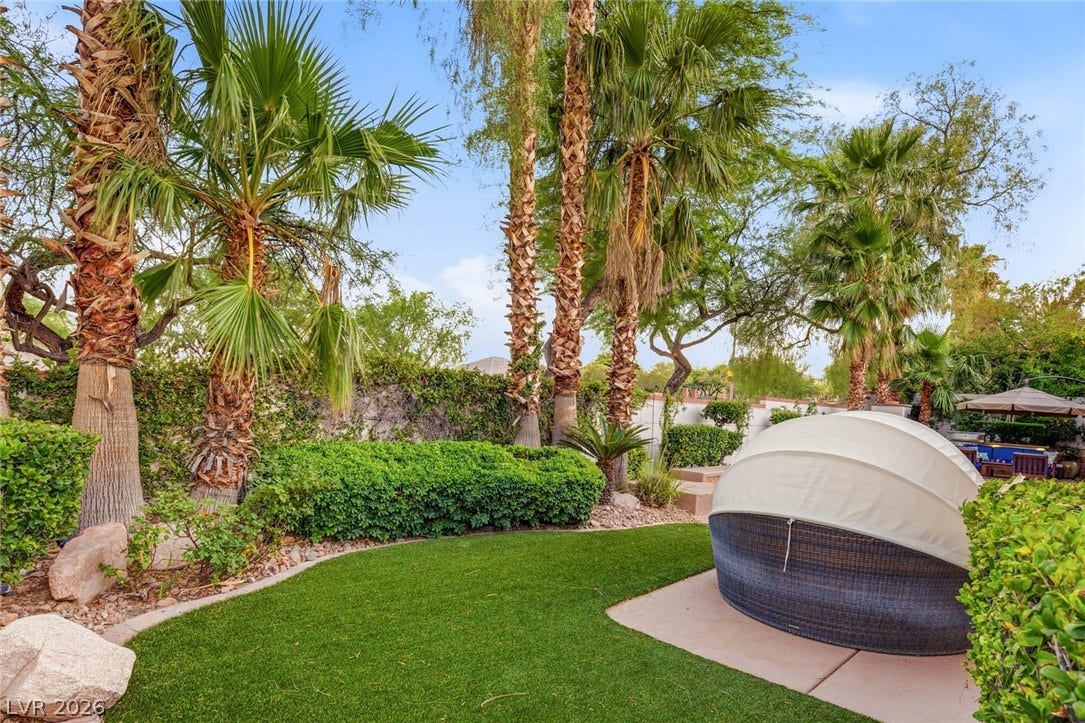 Towering palm trees and manicured hedges frame a private grassy backyard oasis.
