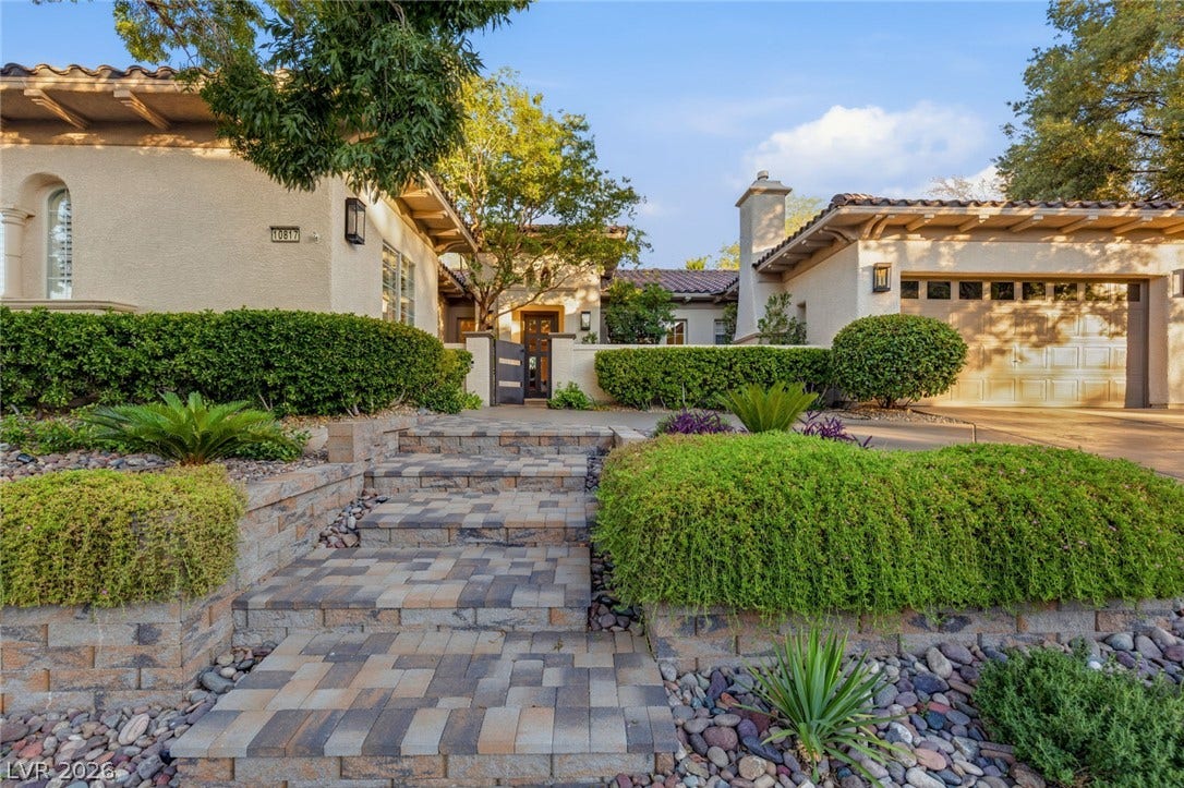 Stone paver steps lead to a gated entryway framed by stucco walls and tile roofing.