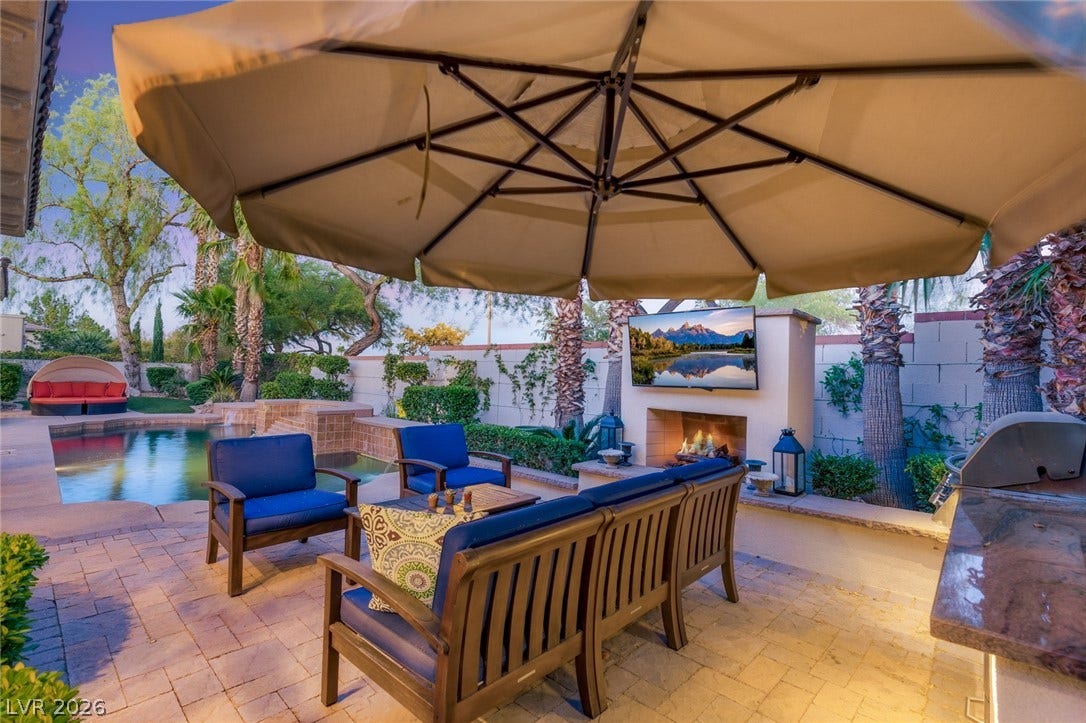An inviting stone patio integrates an outdoor fireplace, built-in kitchen, and adjacent swimming pool.