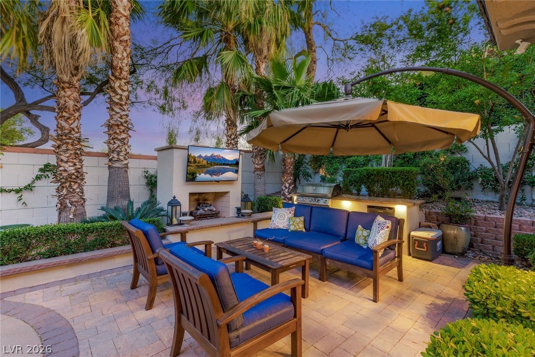 Lush palm trees frame a paved patio complete with an integrated outdoor kitchen and fireplace.