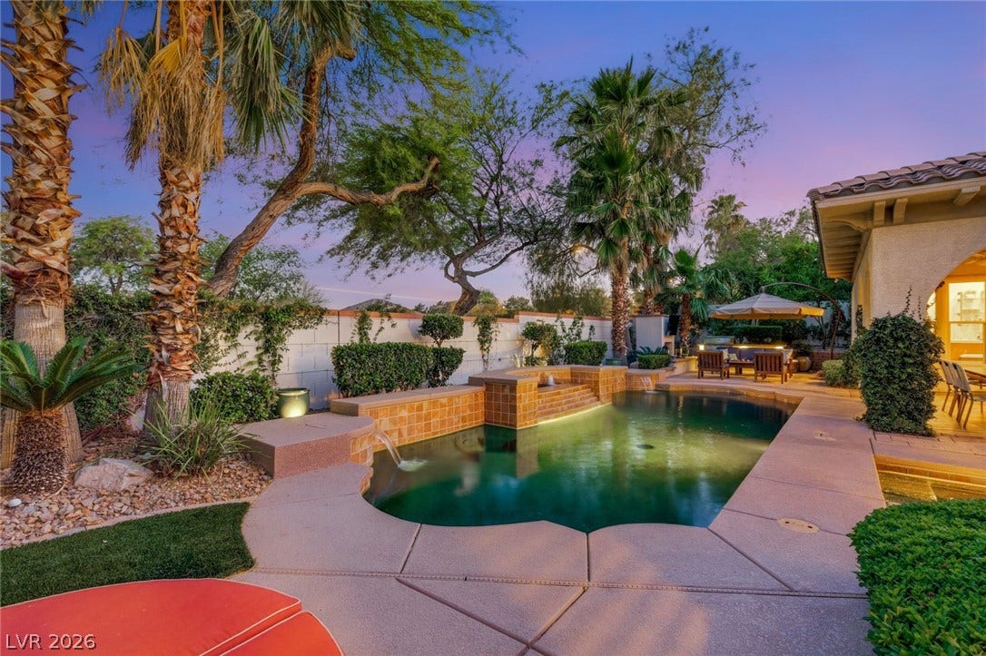 Mature palms frame a sparkling backyard swimming pool with a cascading water feature.