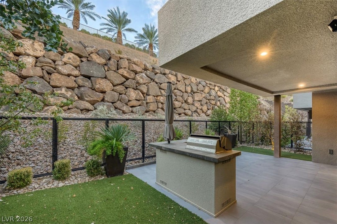 Sheltered outdoor kitchen overlooks a private yard bounded by a natural stone retaining wall.
