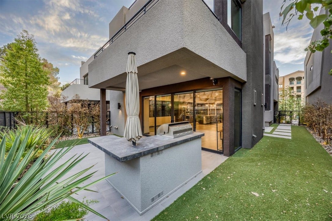 An outdoor kitchen prep island anchors the private patio next to a manicured lawn.