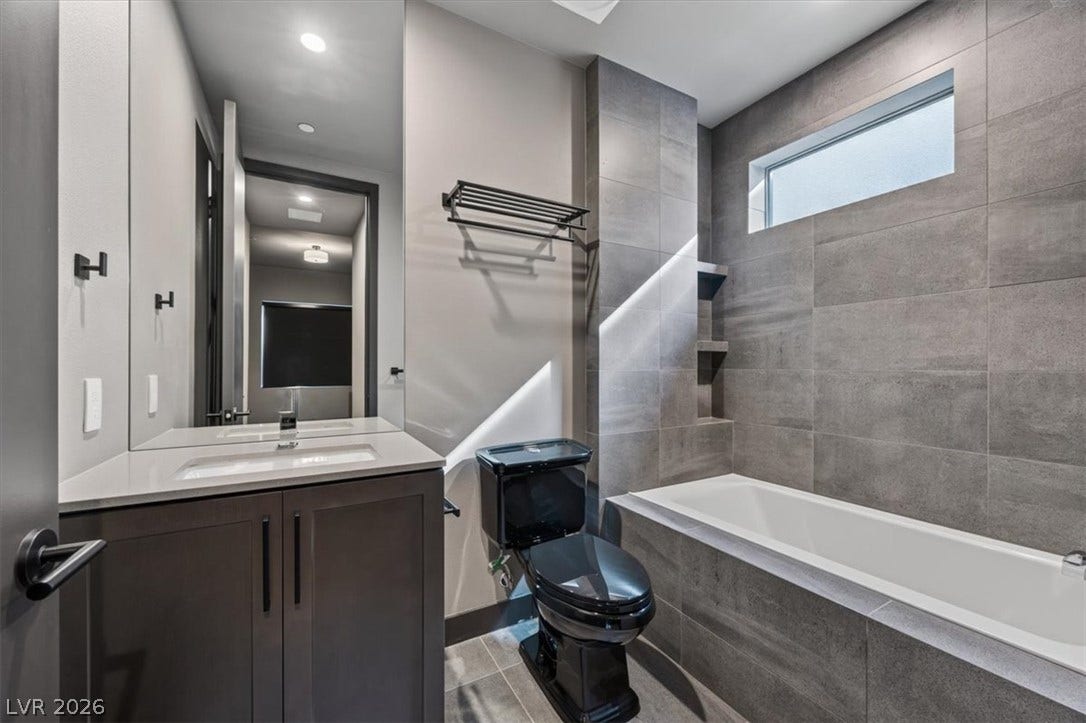A modern bathroom features clean-lined tiling, a deep soaking tub, and a sleek dark vanity.