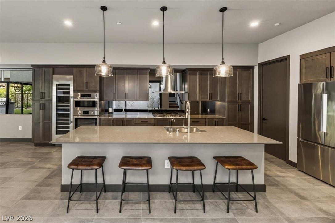 A spacious kitchen anchor with sleek stone countertops and extensive cabinetry over neutral tile flooring.