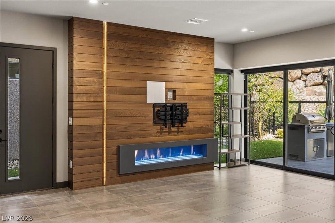 Warm wood paneling frames a linear fireplace beneath recessed lighting and sliding glass doors.
