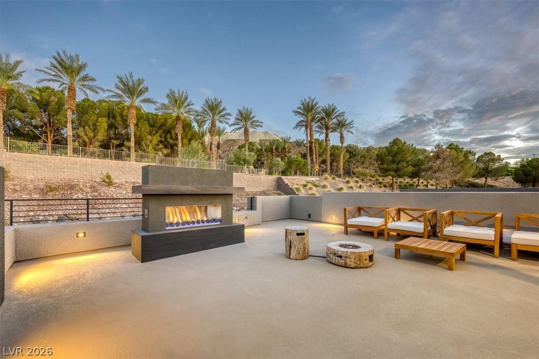 An outdoor fireplace anchors this expansive concrete patio with scenic mountain and palm tree views.