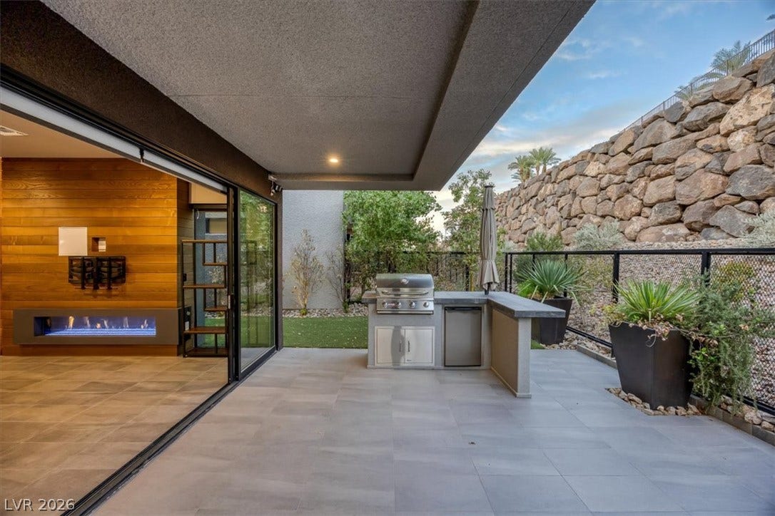 Seamless indoor-outdoor living transitions effortlessly to a covered patio with built-in barbecue and stone accents.