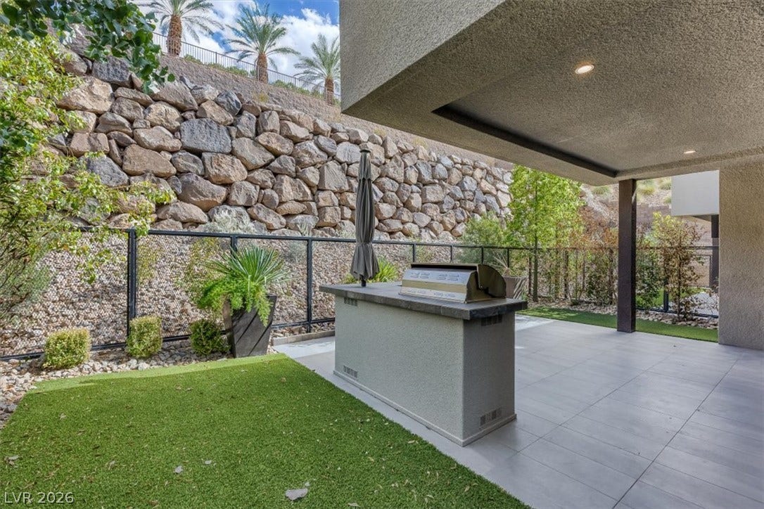 A covered stone patio opens to an outdoor kitchen and a beautifully retained hillside yard.