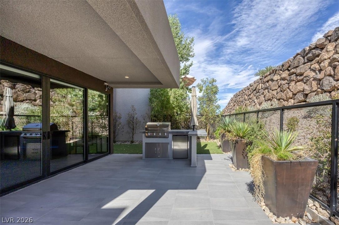 Stone pavers line a covered terrace equipped with a built-in outdoor kitchen and glass doors.