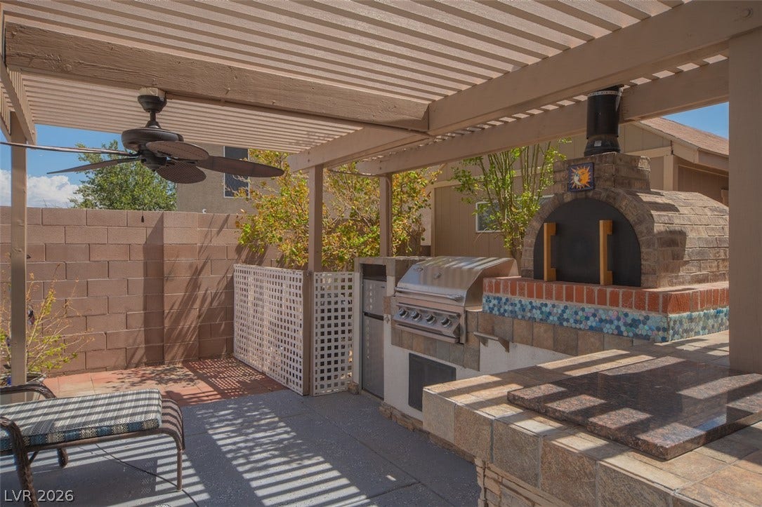 121 Heather Drive, Henderson, NV 89002 An outdoor kitchen with built-in barbecue and pizza oven sits under a shaded pergola.