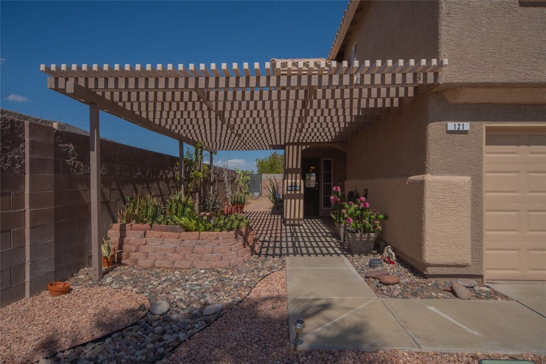 121 Heather Drive, Henderson, NV 89002 A spacious pergola-covered entry patio features stone garden beds alongside the concrete walkway.