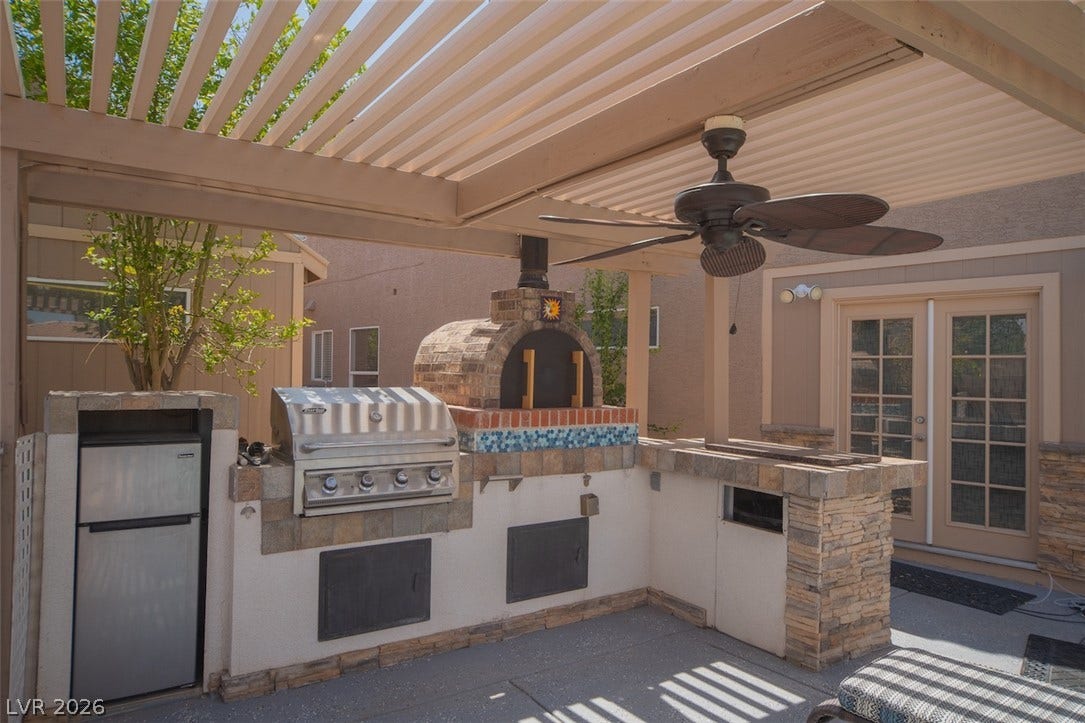 121 Heather Drive, Henderson, NV 89002 An outdoor kitchen features a built-in barbecue and brick pizza oven under a shaded pergola.