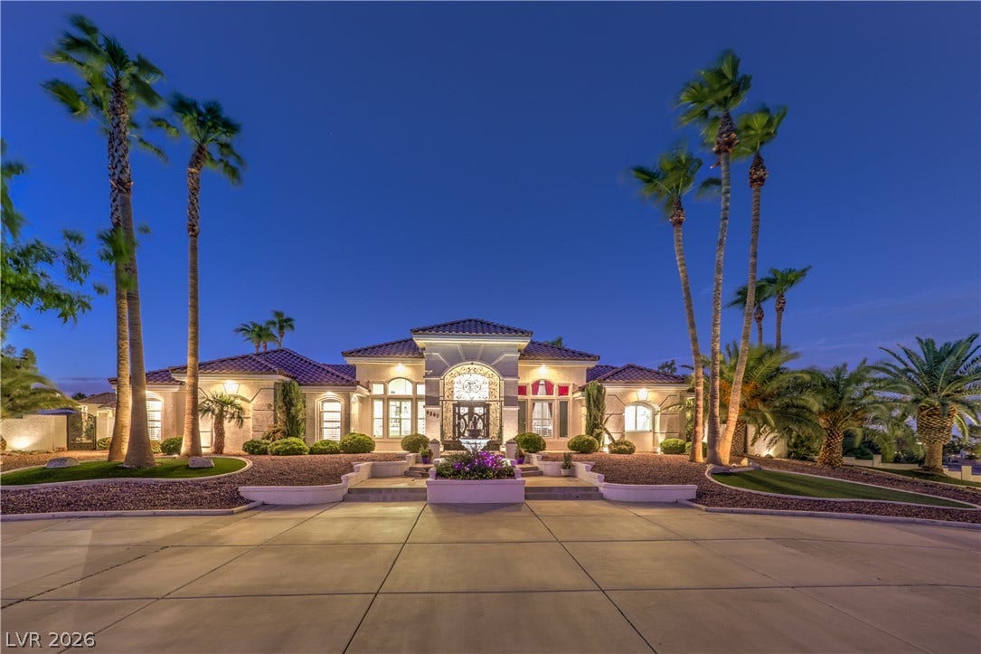 Elegant arches and a grand driveway define this luxurious custom estate under palm trees.