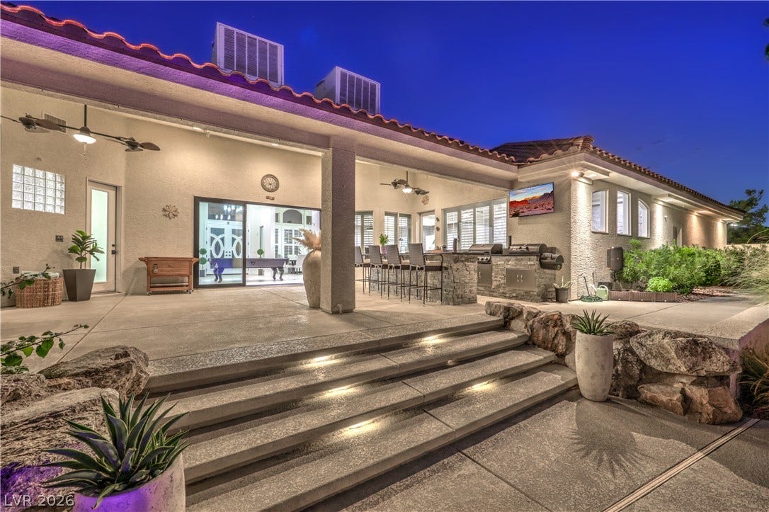 An expansive covered patio features integrated concrete steps, a built-in outdoor kitchen, and tile roofing.