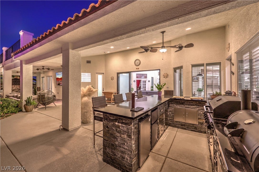 An inviting covered outdoor kitchen features stone accents and a concrete patio floor.