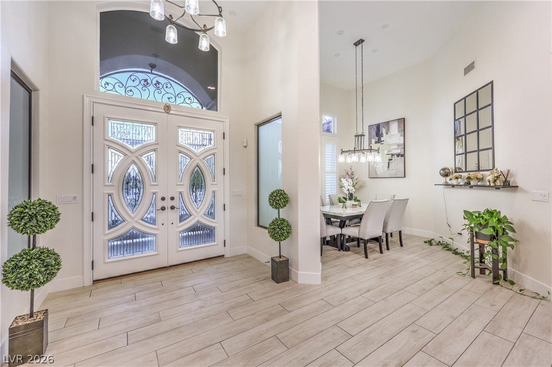 Double entry doors lead into a light-filled foyer featuring tile flooring and soaring ceilings.