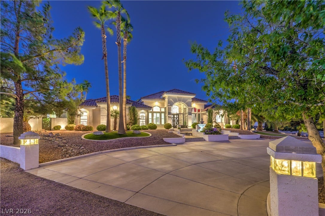 A grand concrete driveway sweeps toward the elegant exterior of this tile-roofed estate.