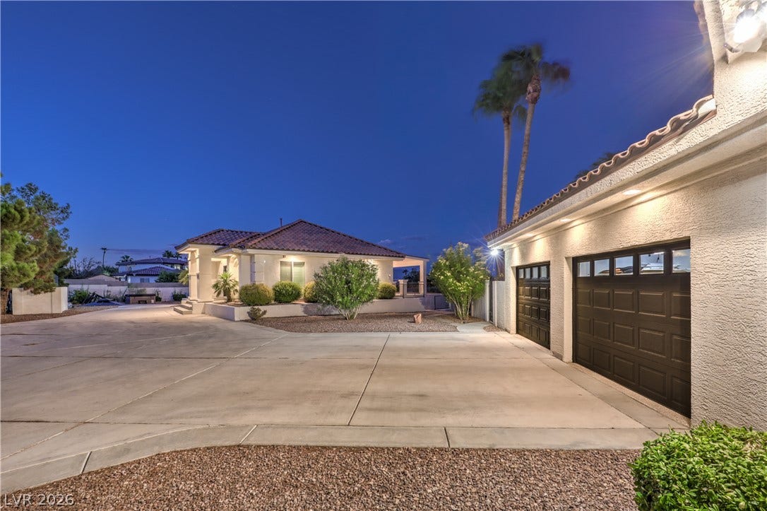 An expansive concrete driveway leads past the detached garage toward a stucco home under desert skies.