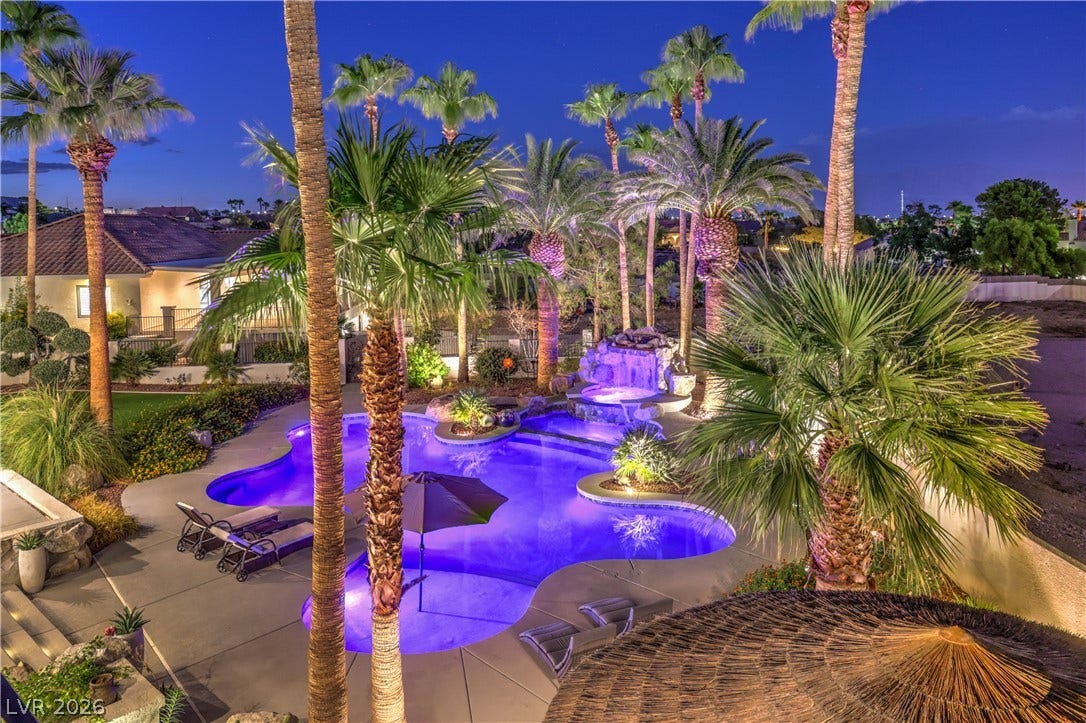 Lush palm trees surround an inviting swimming pool and spa illuminated under the evening sky.
