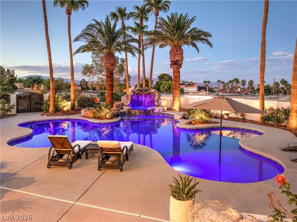 Palm trees frame a customized swimming pool complete with an integrated stone waterfall feature.
