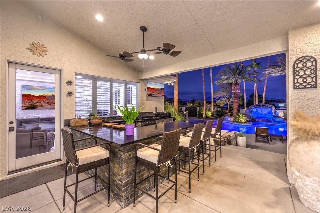 A spacious covered patio overlooks the sparkling pool with tropical landscaping and waterfall features.