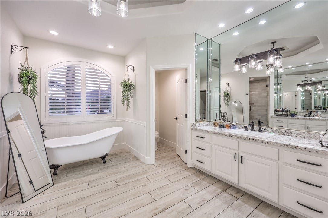 An elegant soaking tub sits beneath an arched window alongside a stone-topped vanity.