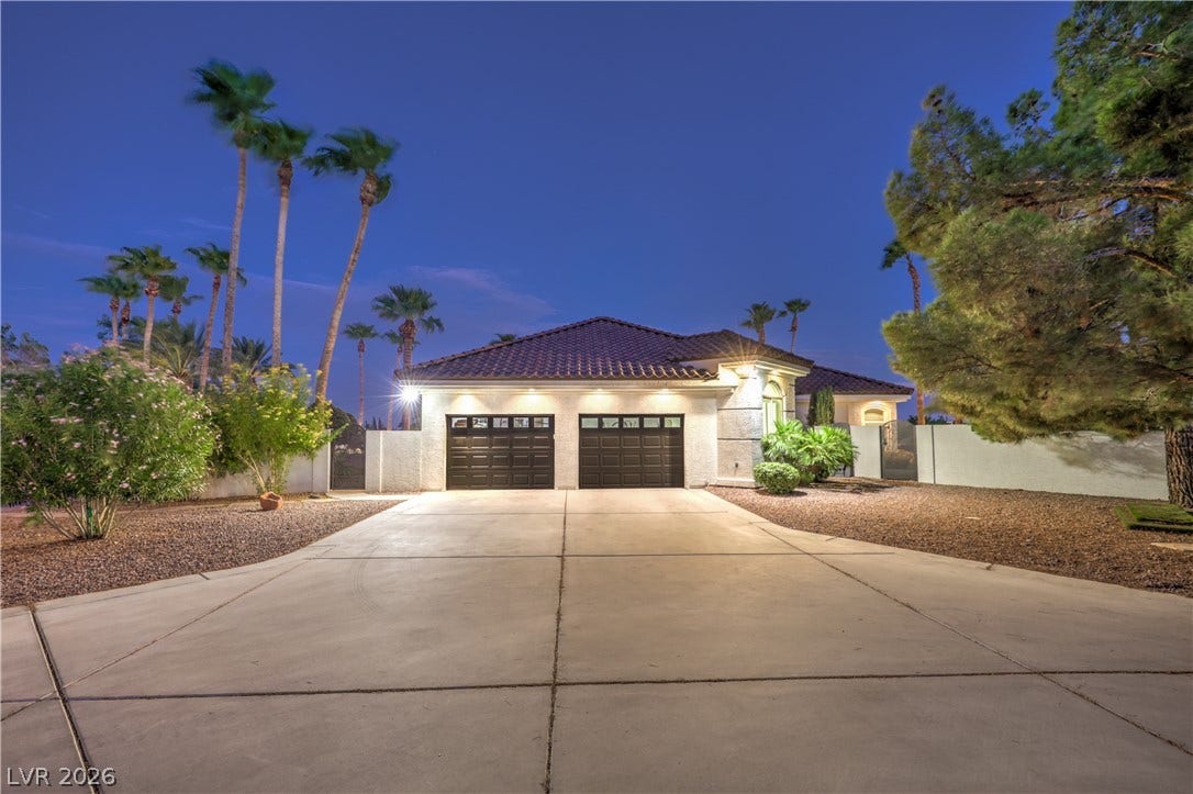 An expansive concrete driveway leads directly to a modern three-car garage under a twilight sky.