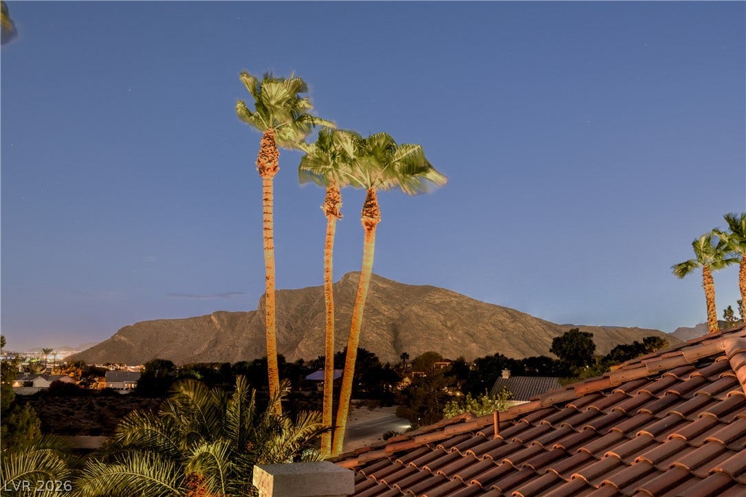 Dramatic mountain vistas rise behind swaying palms and classic tile roofing.