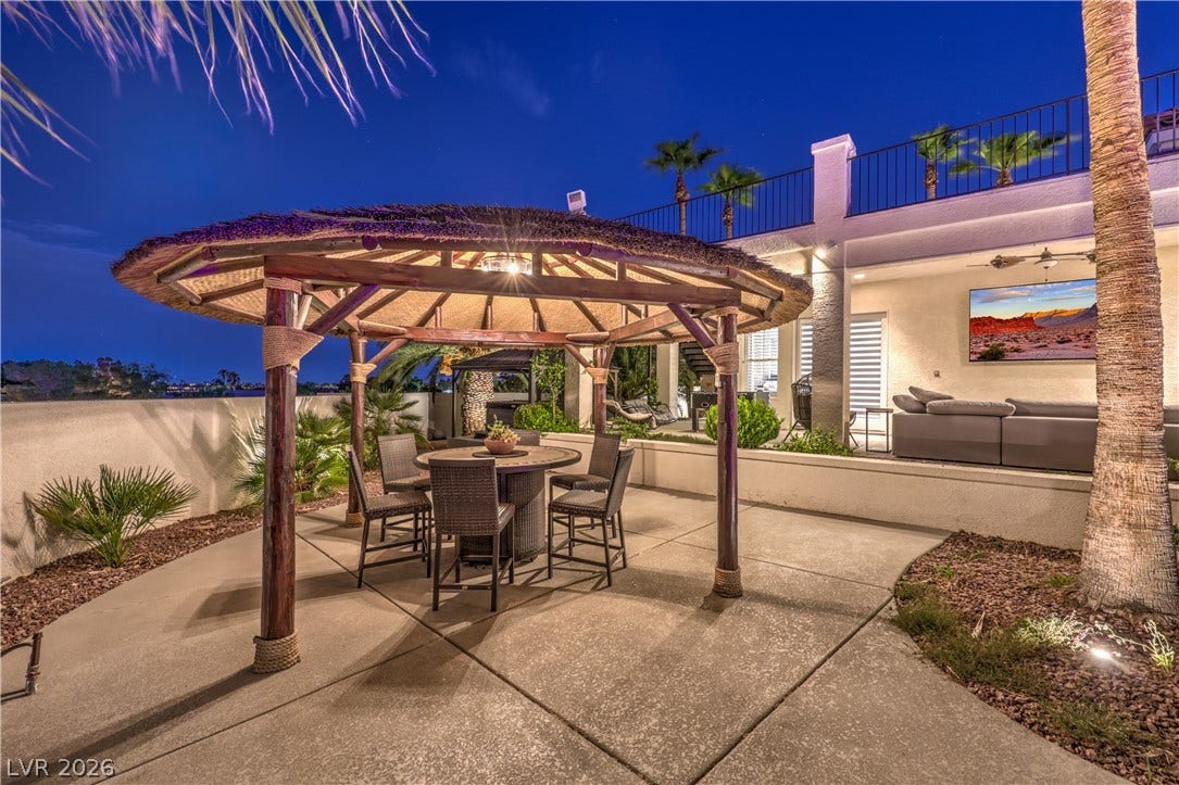 An inviting backyard patio features a thatched gazebo alongside concrete flooring and a covered lounge area.
