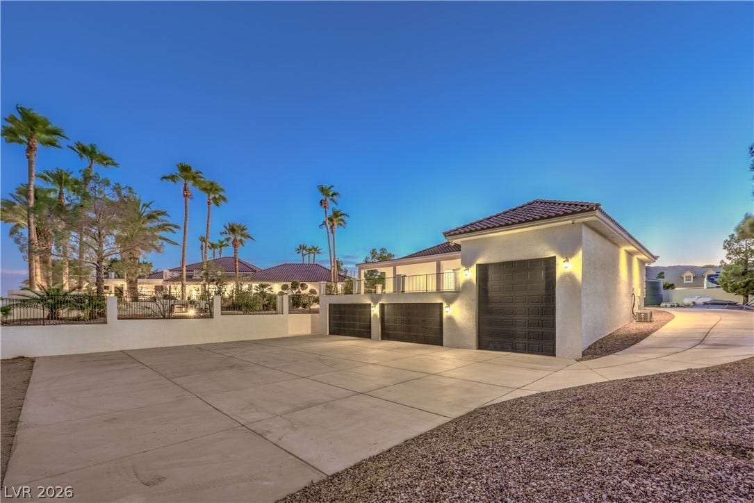 A spacious concrete driveway leads toward multi-car garage bays under a tiled roof.