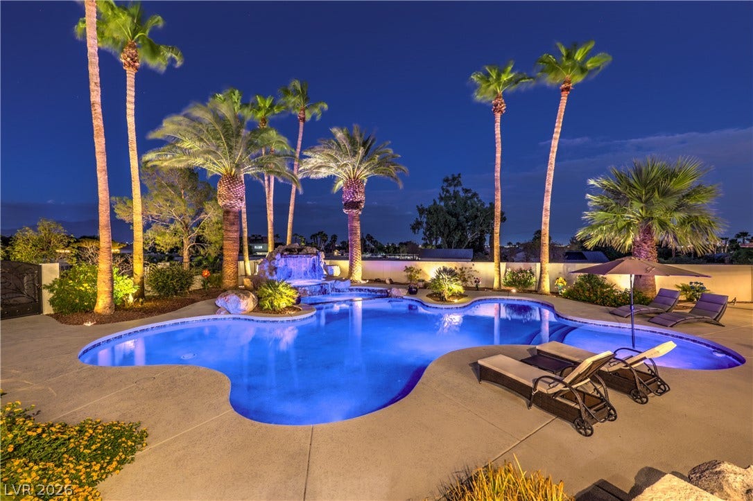 Lush palm trees and integrated stone waterfalls frame a glistening backyard swimming pool.
