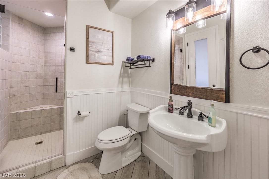 A pedestal sink, classic wainscoting, and a tiled walk-in shower define this bath.
