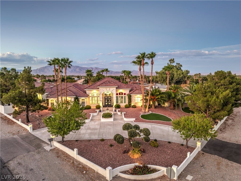 A grand paved driveway sweeps toward this elegant tile-roof estate framed by desert landscaping.