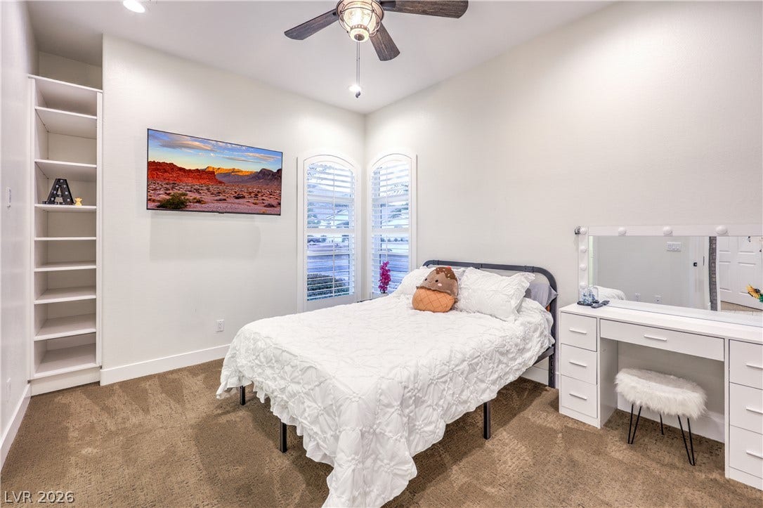 High ceilings and arched windows with plantation shutters enhance this carpeted bedroom.