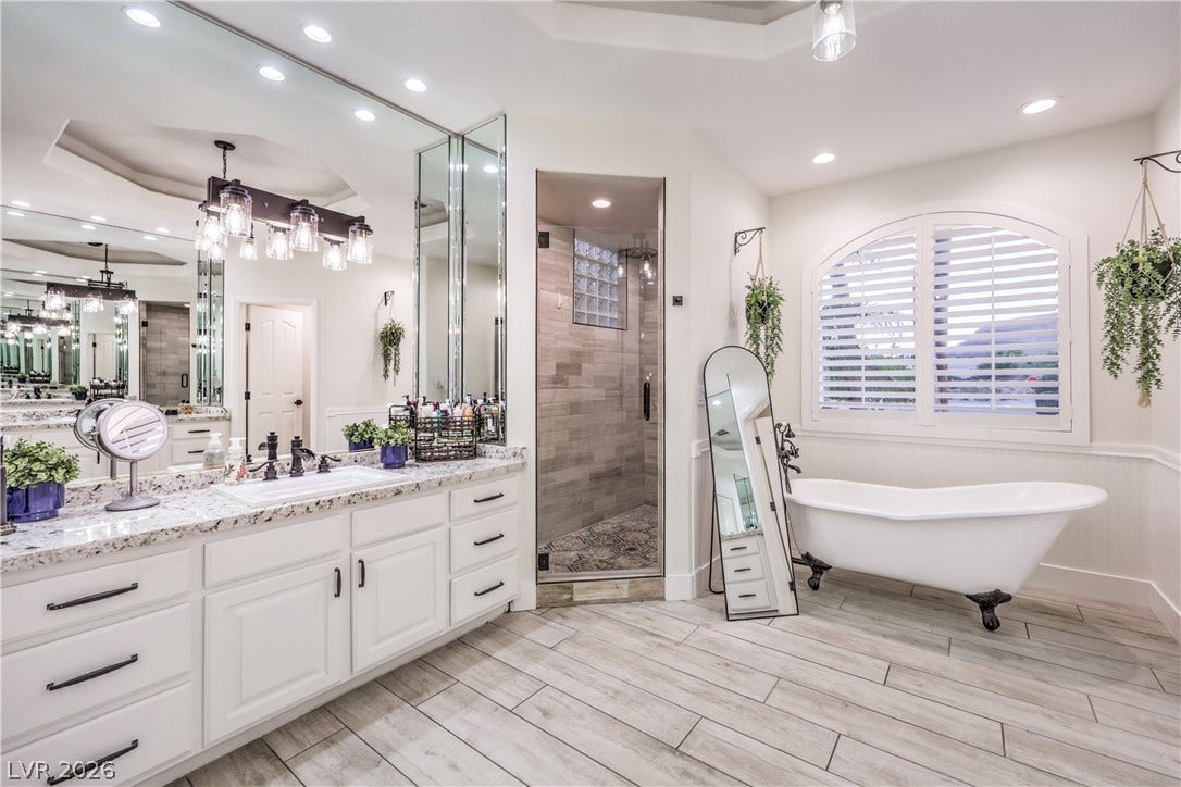 An elegant clawfoot tub sits beside a large arched window in this spacious bathroom.