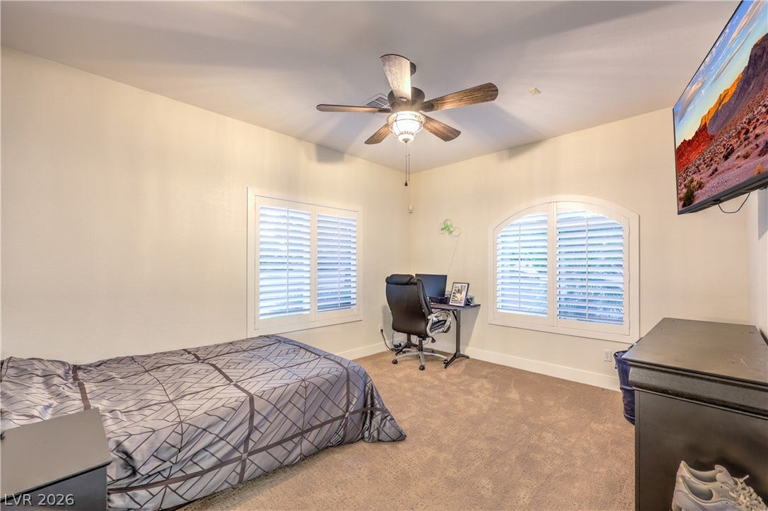 Plentiful natural light streams through plantation shutters onto soft carpeting in this comfortable room.