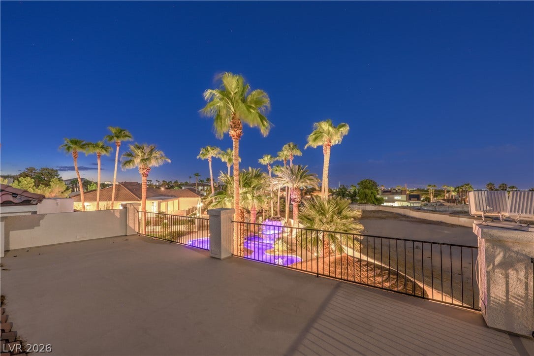 An elevated terrace overlooks a illuminated resort-style swimming pool lined with mature palm trees.