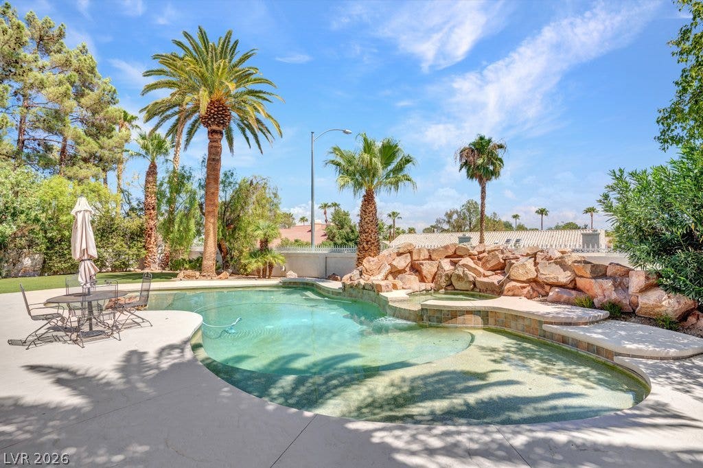 1632 Marbella Ridge Court, Las Vegas, NV 89117 Lush palm trees and natural rock formations surround a private swimming pool under sunny skies.
