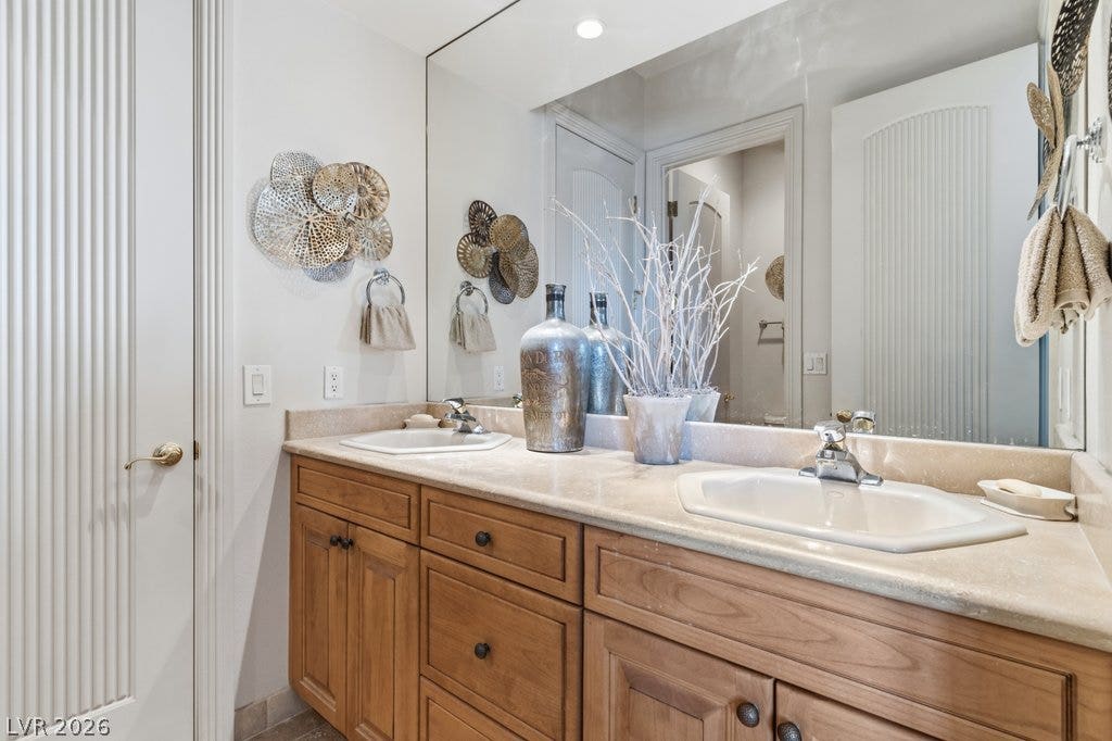1632 Marbella Ridge Court, Las Vegas, NV 89117 Warm wood cabinetry and neutral stone counters anchor this comfortable dual vanity bathroom.