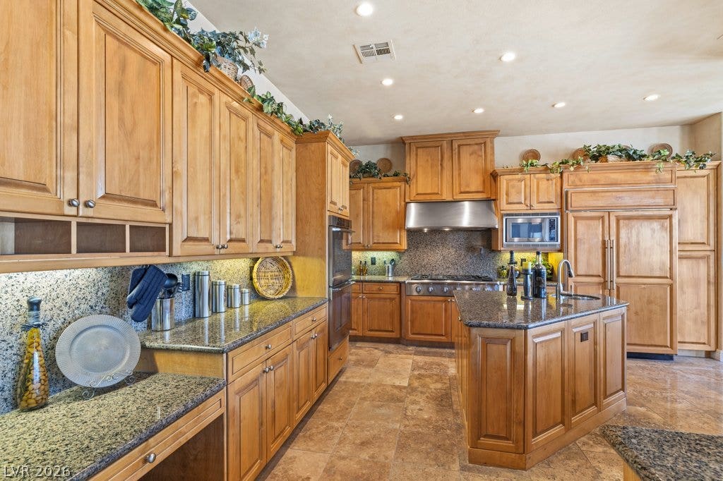 1632 Marbella Ridge Court, Las Vegas, NV 89117 Rich wood cabinetry and polished stone countertops elevate this expansive culinary space.